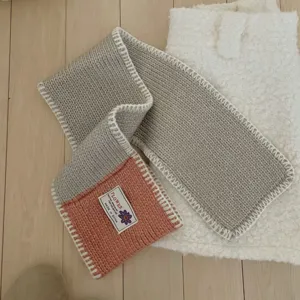 Detailed view of color block knitted wool blend scarf with white edge stitching and brand label.