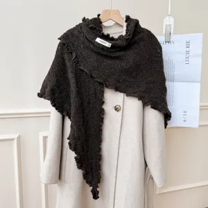 Dettaglio scialle triangolare a maglia marrone scuro con volant su cappotto, elegante.