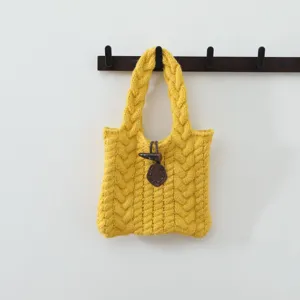 Gros plan détaillé sur la texture en tricot torsadé du sac à main jaune et son attache.