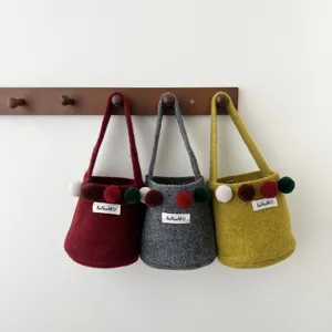 Vue détaillée de sacs-seaux en feutre faits main avec des pompons colorés sur un support.