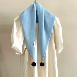 Vue détaillée d'une écharpe triangulaire en tricot bleu clair avec des pompons.