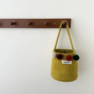 Vue détaillée d'un sac seau en feutre jaune-vert stylé avec de charmants pompons colorés.