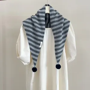Vue détaillée d'une écharpe triangulaire en tricot rayé gris avec des pompons.