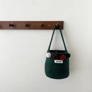 Vue détaillée d'un élégant sac seau en feutre vert foncé avec des pompons colorés.