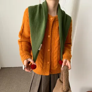 Vue détaillée de l'écharpe triangulaire en laine verte avec des pompons et un cardigan.