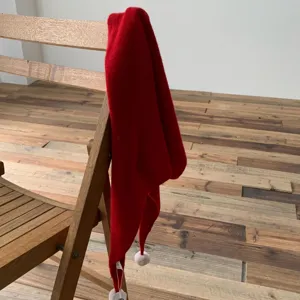 Vue détaillée d'une écharpe triangulaire rouge en tricot avec des pompons sur une chaise.