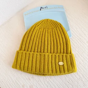 Detail de bonnet en maille cotee jaune, chapeau d'hiver en laine avec petite plaque.