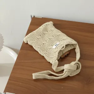 Détail de sac bandoulière en tricot avec motif torsadé, bouton olive et petite étiquette.