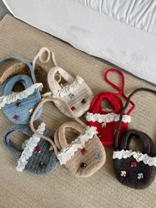 Nahaufnahme von gestrickten Kindertaschen mit Spitzenbesitz und süßen Pilz-Details auf Teppich.