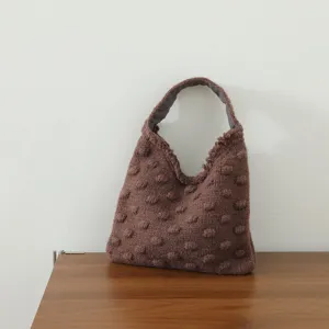 Gros plan sur le sac à main en tricot marron avec texture 3D de pompons et tissage doux.