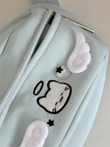Close-up detail of cute cat embroidery sling bag with plush wings and green fabric.