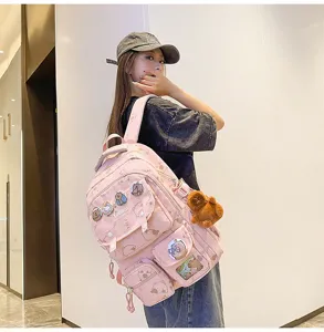 Dettaglio zaino rosa con capibara cartoon, grande borsa scolastica con spille e grazioso ciondolo.