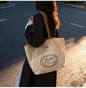Gros plan sur le sac cabas en toile beige avec anses en cuir marron et design de poche imprimé.