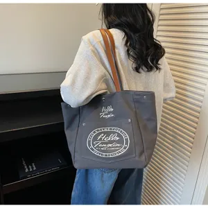 Vue détaillée du sac cabas d'épaule en toile gris foncé avec anses marron et texte.