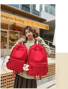 Detailed view of a stylish red canvas backpack with front pocket and cute bear charm.