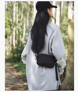 Casual black crossbody bag worn outdoors, showing zipper pockets and adjustable straps.