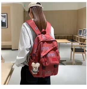Stylish red backpack for students with letter prints and cute bear pendant detail.