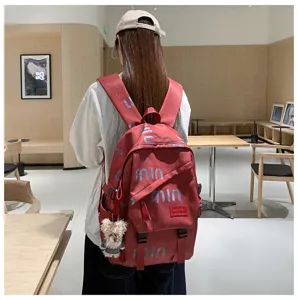 Red canvas backpack detail showing stylish letter print and cute bear pendant in cafe scene.