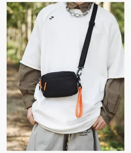 Detail shot of black casual crossbody bag with orange strap, outdoor street style fashion.