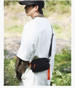 Close-up detail shot of black casual crossbody bag with orange strap accents worn outdoors.