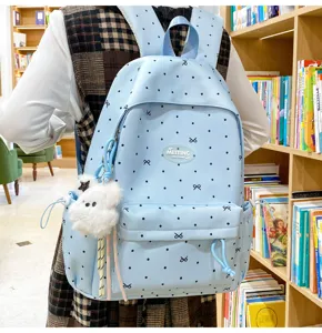 Detailed view of light blue polka dot backpack with cute bow print and fluffy bear pendant.