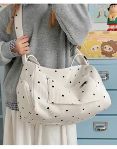 Detailed view of white corduroy shoulder bag with black polka dots and front zipper pocket.