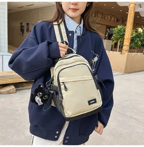 Compact beige casual backpack with front pocket and cat pendant for daily commute.