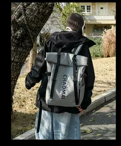 Outdoor street detail view of a large capacity grey roll-top backpack with black straps.