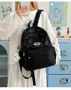 Close-up of cute black star-printed canvas backpack with plush pendant in cozy room setting.