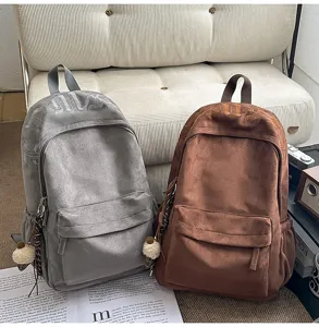 Primo piano di zaini casual in velluto grigio e marrone, con ciondoli graziosi e consistenza.