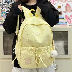 Detail view of the cute yellow student backpack with star pattern and cute pom-pom pendant.