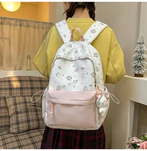 Cute cartoon cat print canvas backpack with pink front pocket and plush pendant for students.