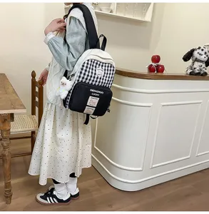 Side view of black and white plaid school backpack in cozy cafe scene with cute pendant detail.