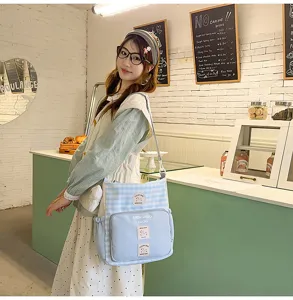 Detail view of the cute blue plaid canvas crossbody shoulder bag with roomy storage and badges.