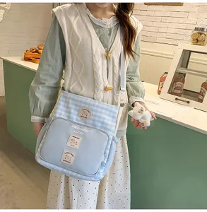 Canvas student shoulder bag with plaid pattern, front pocket, and cute bear pendant detail.