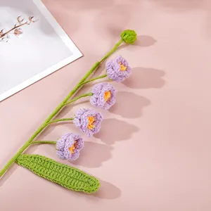 Crochet lily of the valley flower branch detail, handmade wool puff floral decor, soft pink background.