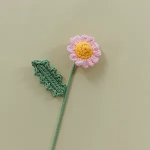 Handmade crochet flower detail shot, cute pink daisy with green leaf, knit craft decor.