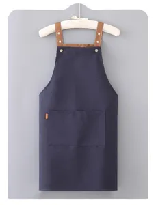 Dettaglio del grembiule in tela blu scuro con spalline marroni e doppie tasche.