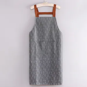 Grembiule da cucina grigio con motivo a foglie bianche, bretelle marroni e doppie tasche.