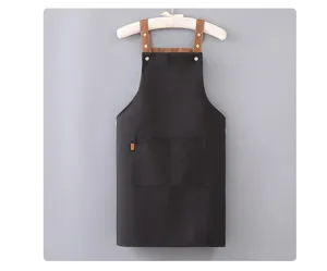 Grembiule da cucina nero in tela con spallacci marroni e doppie tasche anteriori.