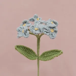 Primo piano di un fiore all'uncinetto blu artigianale con foglie verdi e centro giallo vivace.