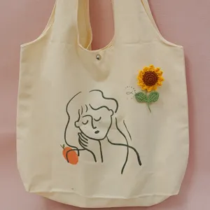 Beige canvas tote bag with minimalist line art print and handmade crochet sunflower decoration.