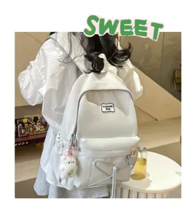 Detail view of the stylish white student backpack with cute pendant and front drawstring pocket.