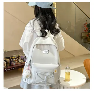 Detailed view of a minimalist white student backpack with cute plush charm and drawstring design.
