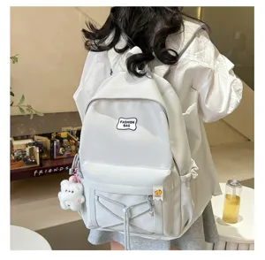 Detail shot of a white student backpack with front bungee cords, cute pendant, and logo patch.