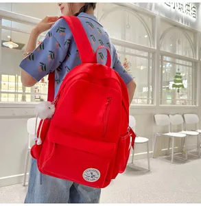 Casual red canvas school backpack detail showcasing front zipper pocket and cute plush pendant.