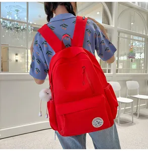 Red canvas backpack detail view showing front zipper pocket, side pouch, and cute plush charm.