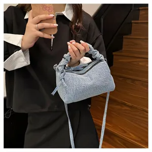 Detail shot of stylish light blue denim ruched handle crossbody bag in indoor setting.