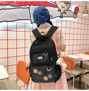 Detail view of black canvas school backpack with clear front pocket, pins, and plush charm.