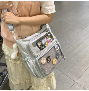 Grey canvas ita bag detail shot, transparent window pocket with cute badges and plush charm.